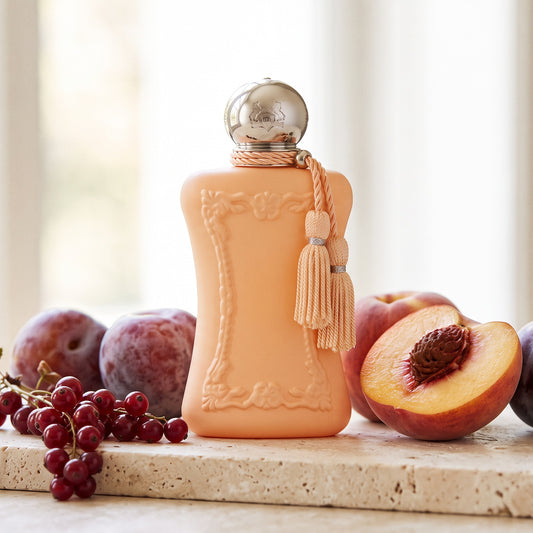 Parfums de Marly Cassili on pale travertine with ripe plums and a halved peach beside a sprig of currants