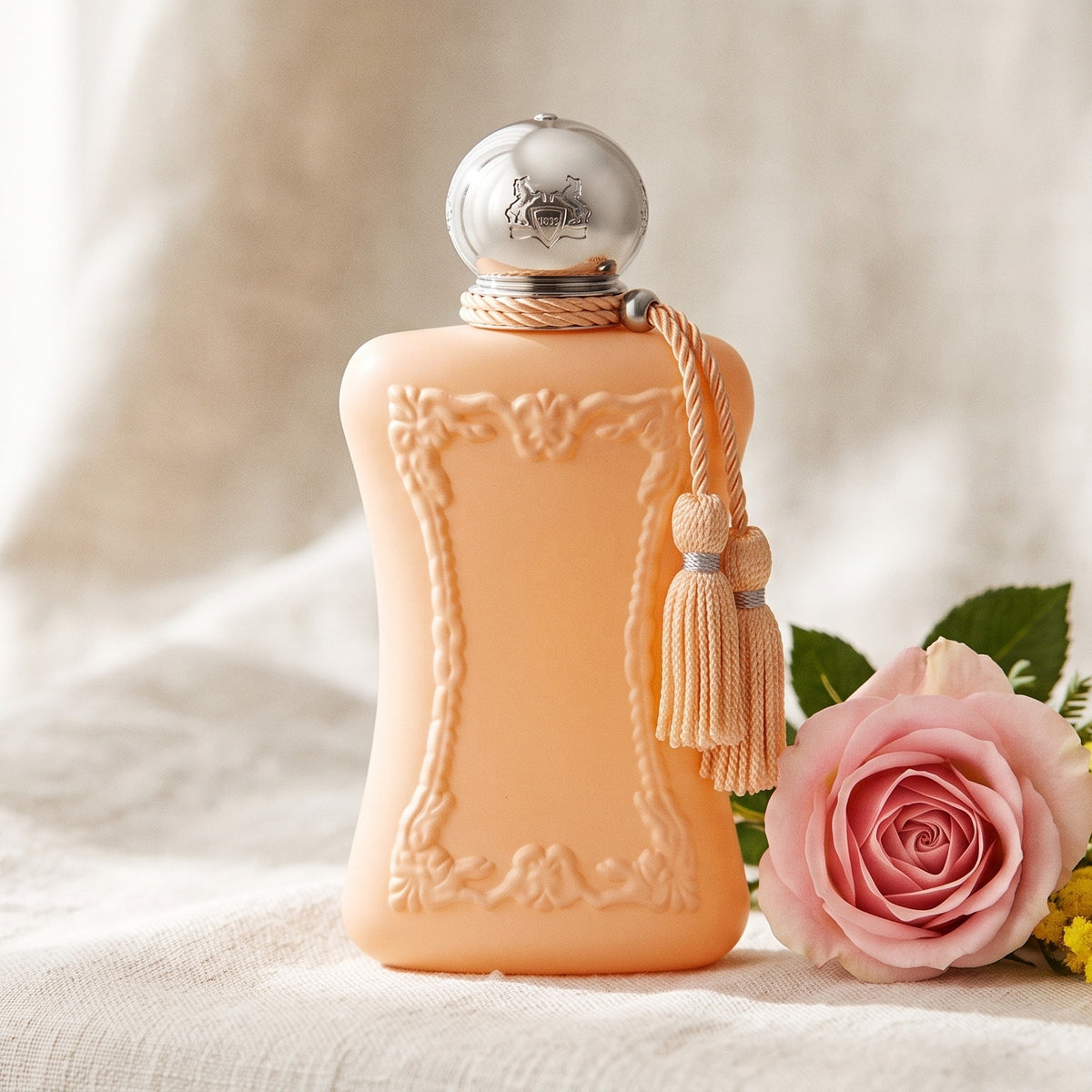 Parfums de Marly Cassili on cream linen with a sprig of yellow mimosa beside a pink rose
