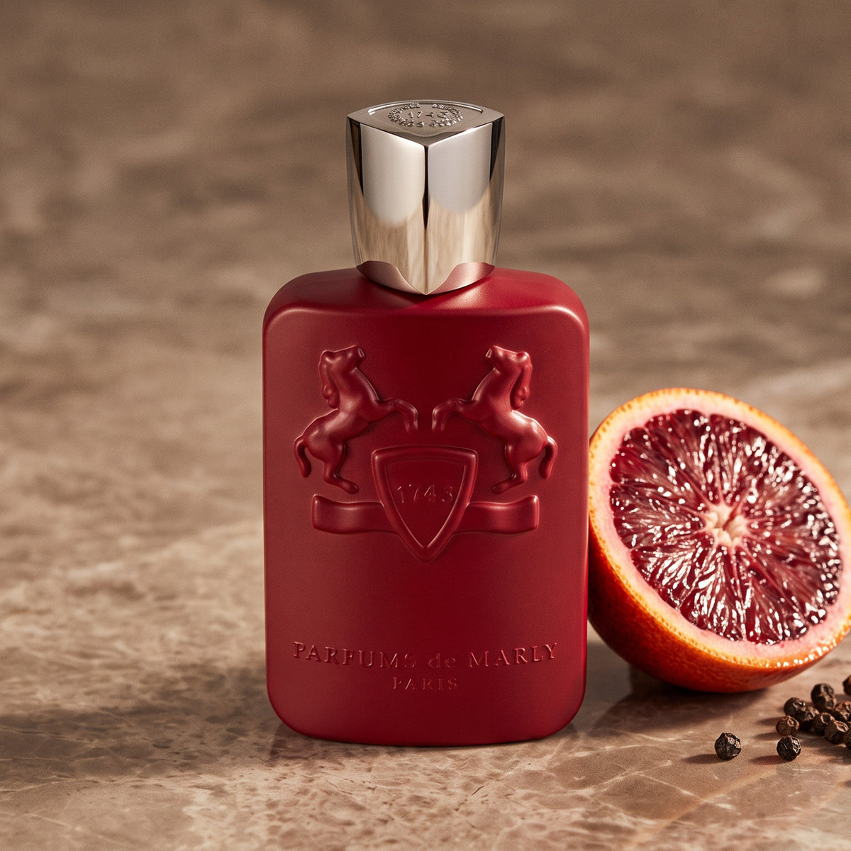 Parfums de Marly Kalan EDP on warm taupe marble with a halved blood orange beside a few black peppercorns
