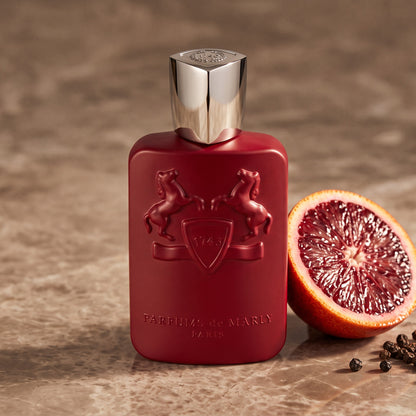 Parfums de Marly Kalan EDP on warm taupe marble with a halved blood orange beside a few black peppercorns