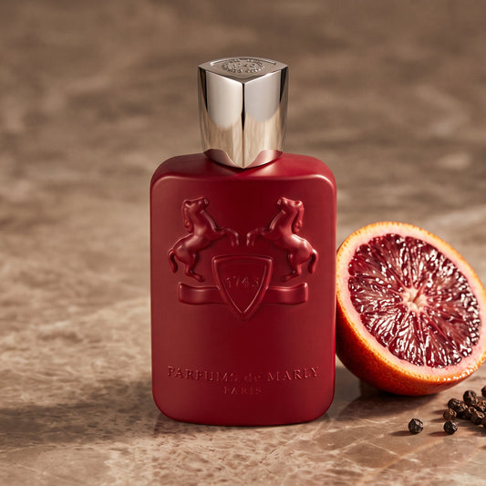 Parfums de Marly Kalan EDP on warm taupe marble with a halved blood orange beside a few black peppercorns