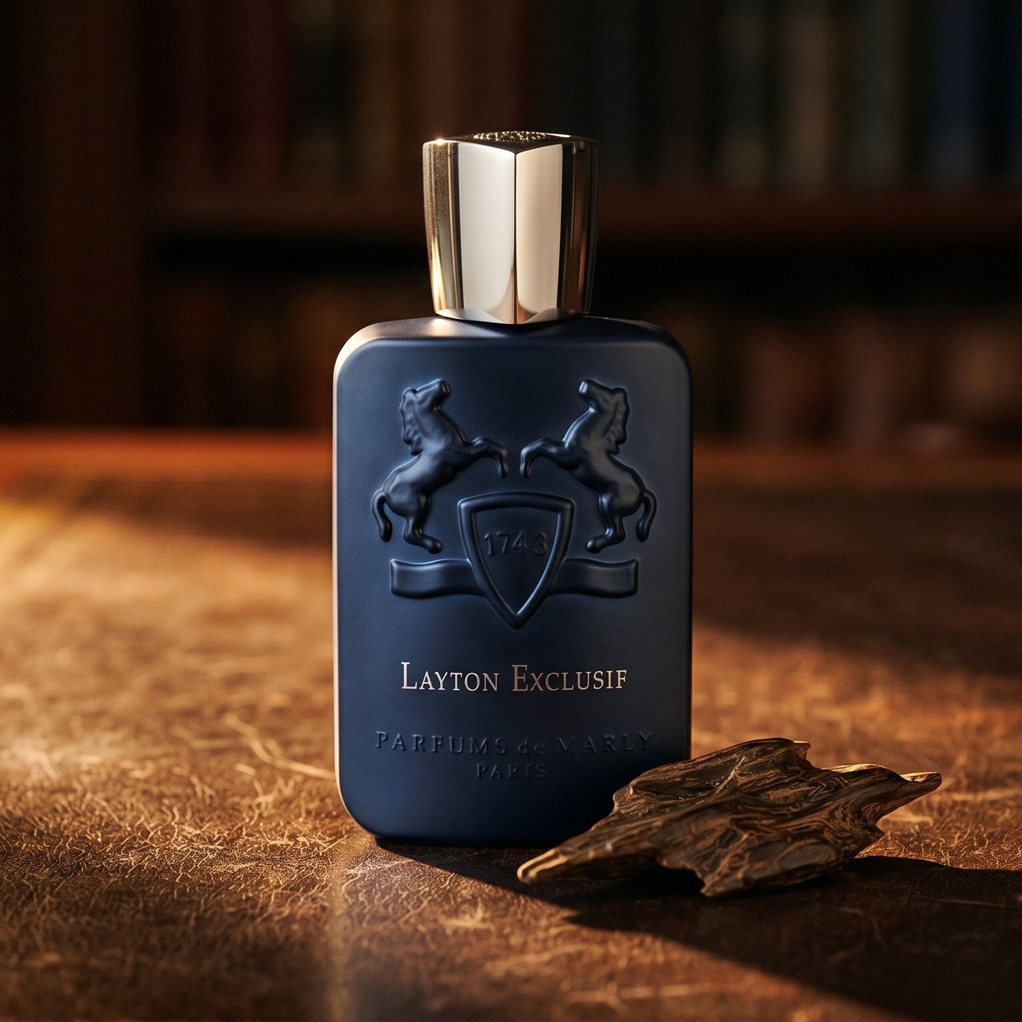 Parfums de Marly Layton Exclusif EDP on dark tan leather desk with a brass lamp casting a warm pool of light