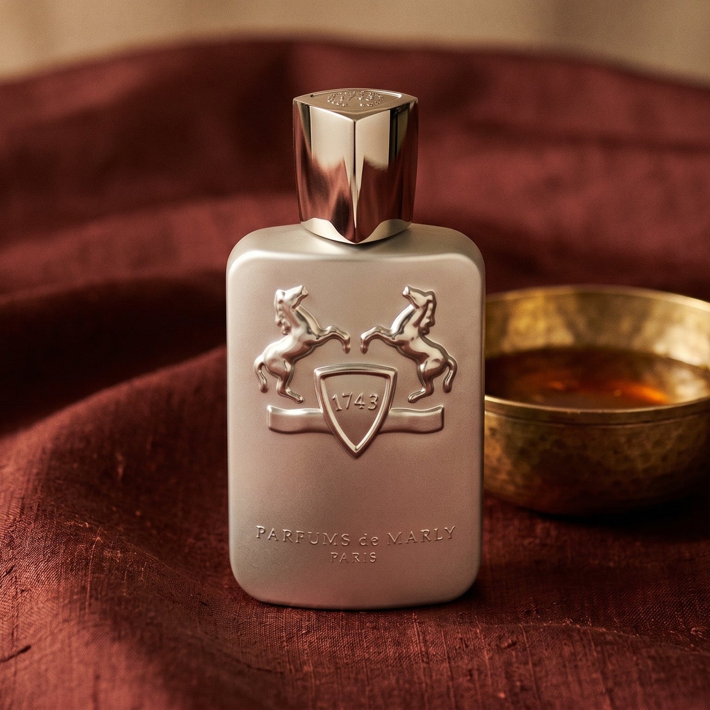 Parfums de Marly Pegasus on amber-toned satin with a gold-rim ceramic dish of labdanum
