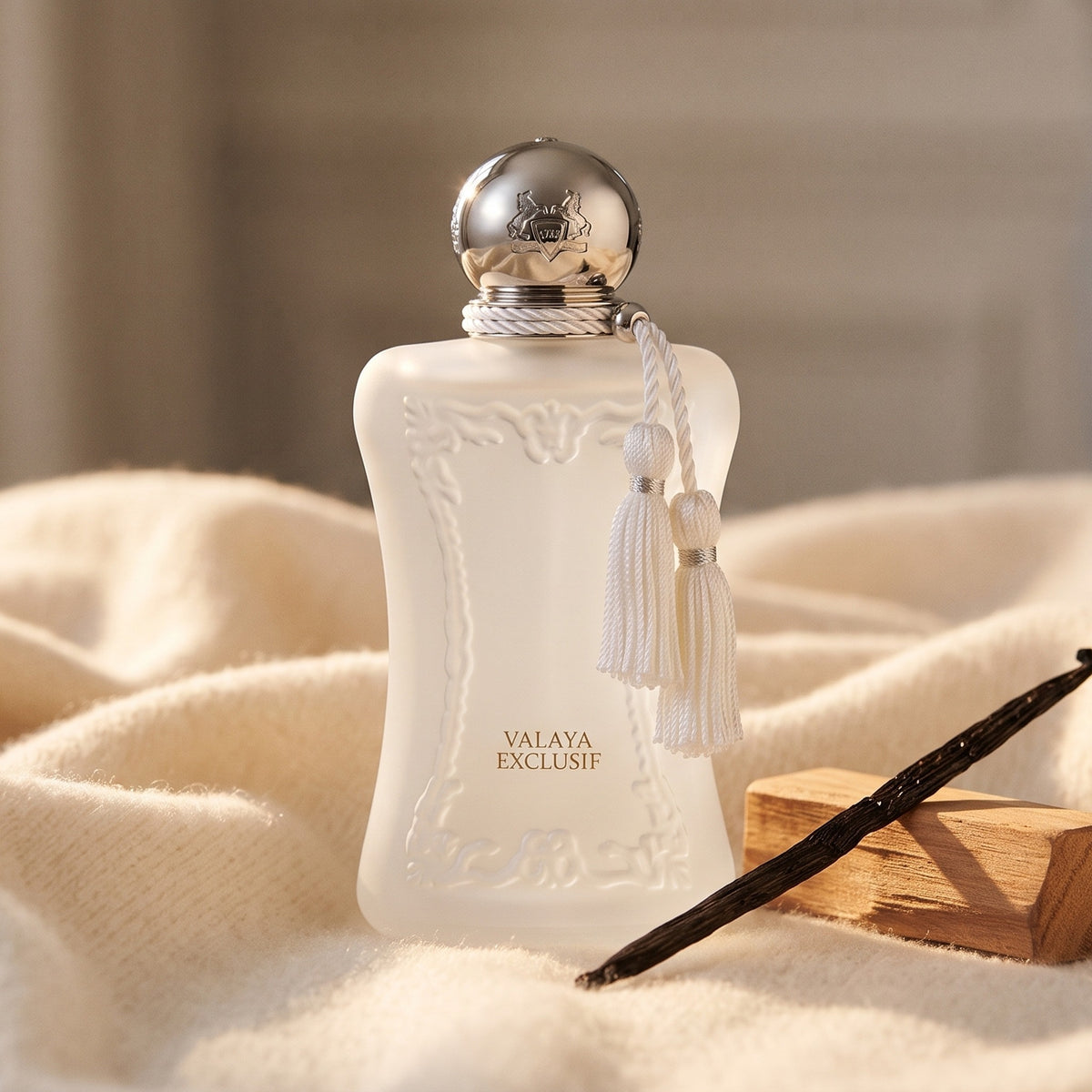 Parfums de Marly Valaya Exclusif EDP on cream cashmere with a vanilla pod beside a small sandalwood block