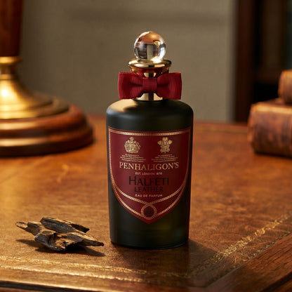 Penhaligon's Halfeti Leather EDP on dark tan leather desk with a brass lamp casting a warm pool of light