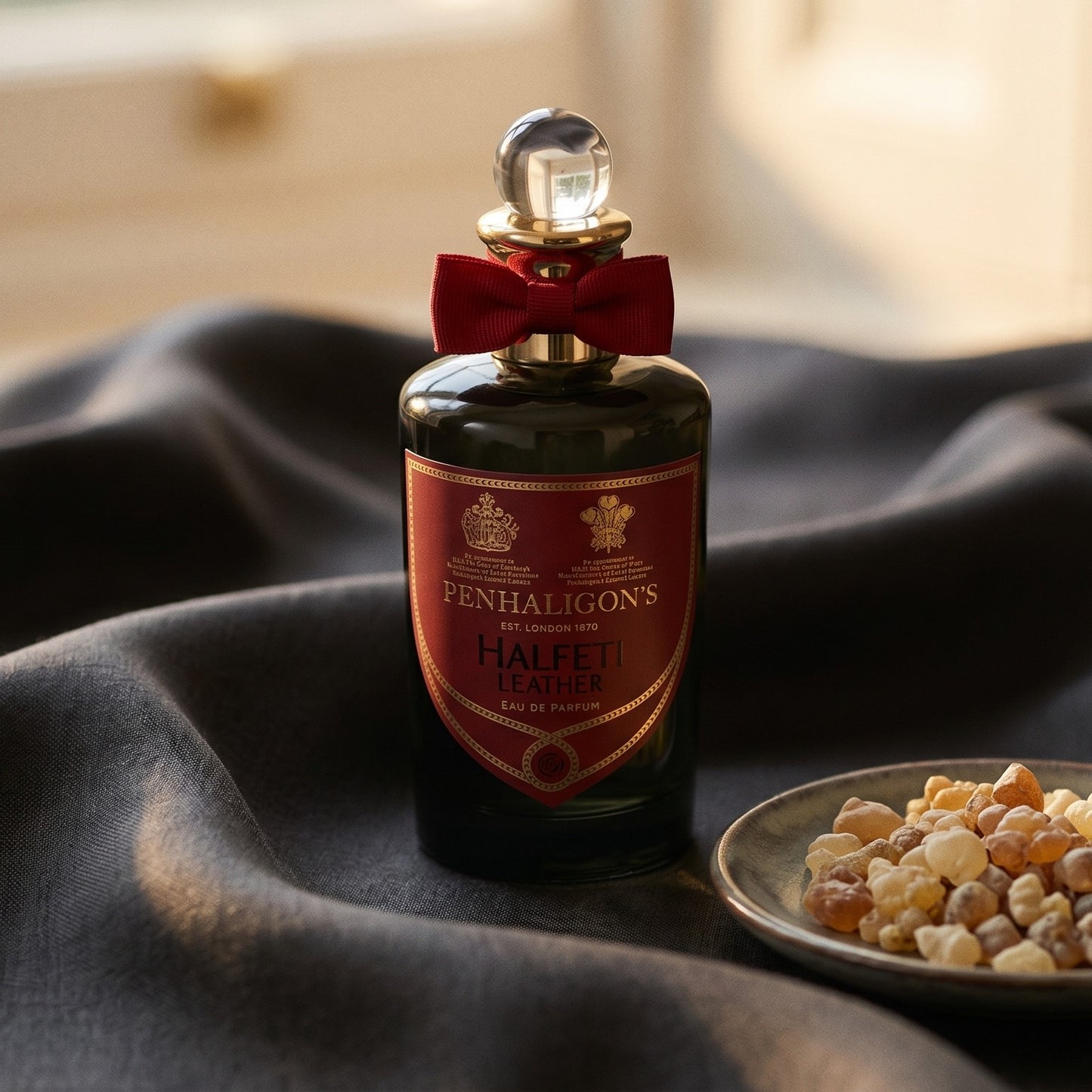 Penhaligon's Halfeti Leather EDP on burnt-orange silk with smoldering agarwood on a stone dish