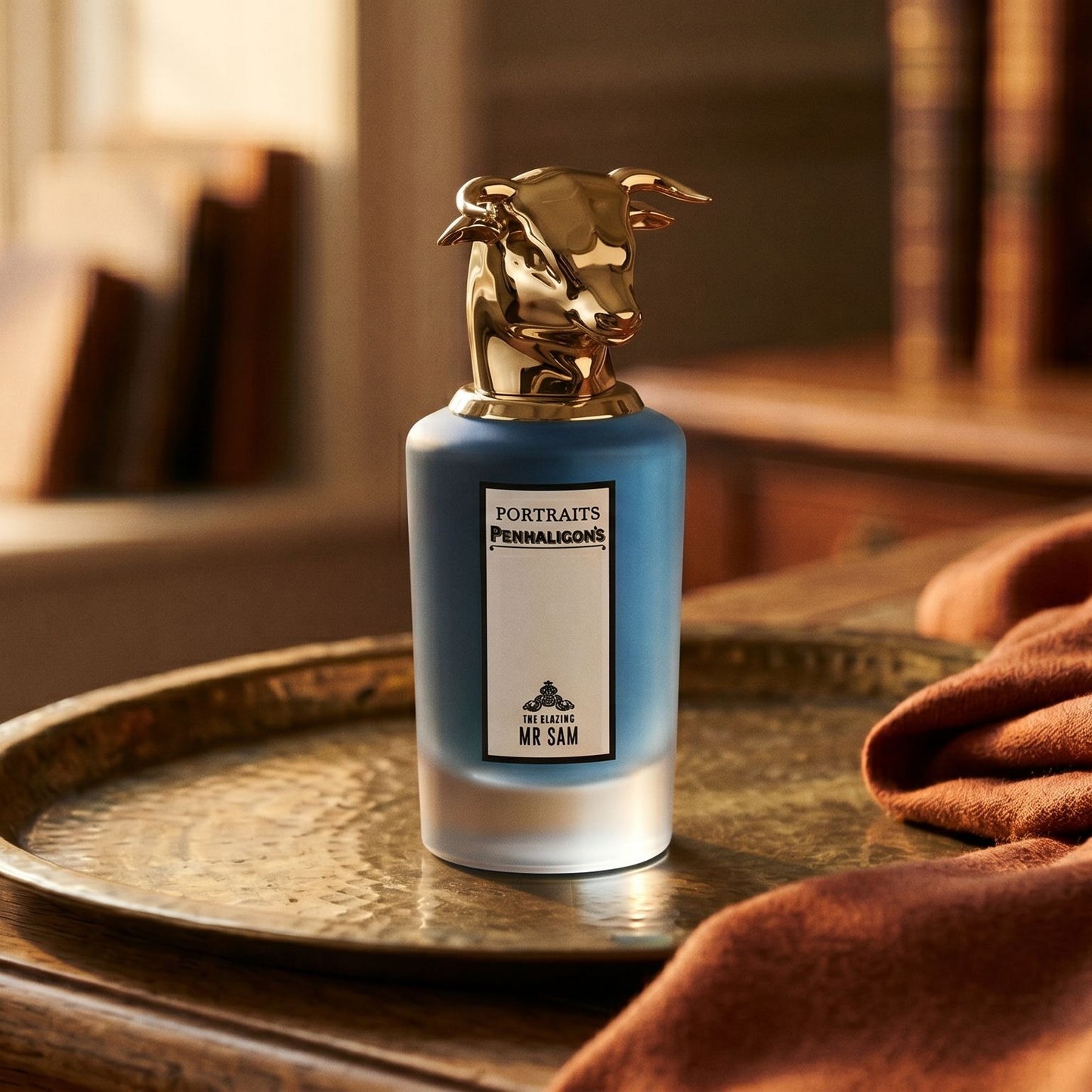 Penhaligon's The Blazing Mister Sam on aged brass tray with a folded pashmina in rust tone