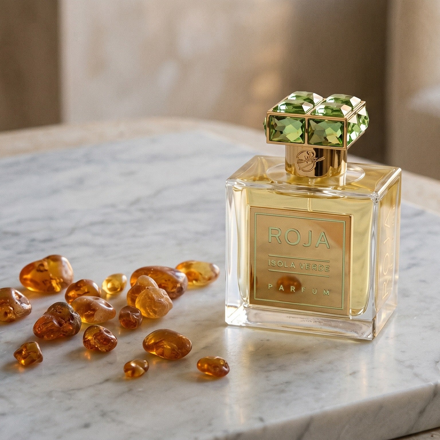 Roja Isola Verde Parfum on pale grey marble with amber resin beads scattered to one side