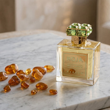 Roja Isola Verde Parfum on pale grey marble with amber resin beads scattered to one side
