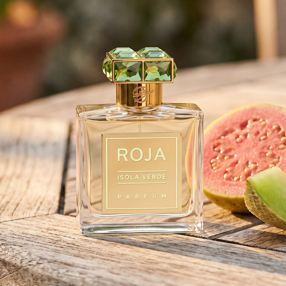 Roja Isola Verde Parfum on sun-bleached teak with a halved guava beside a slice of green melon