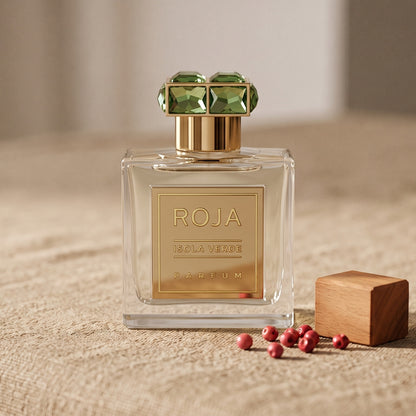 Roja Isola Verde Parfum on sand-coloured linen with a few pink peppercorns beside a small sandalwood block