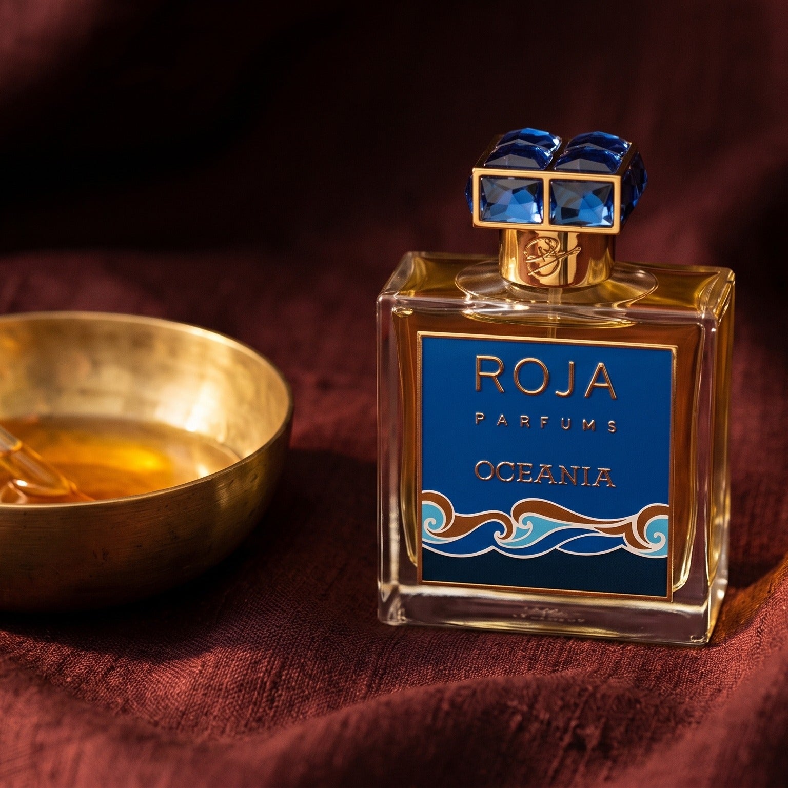 Roja Oceania EDP on amber-toned satin with a gold-rim ceramic dish of labdanum
