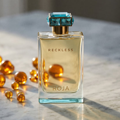 Roja Reckless Pour Femme EDP on cream stone with a scatter of honey-colored ambergris flakes