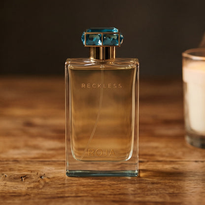 Roja Reckless Pour Femme EDP on walnut side table with a pair of lit votives beside the bottle