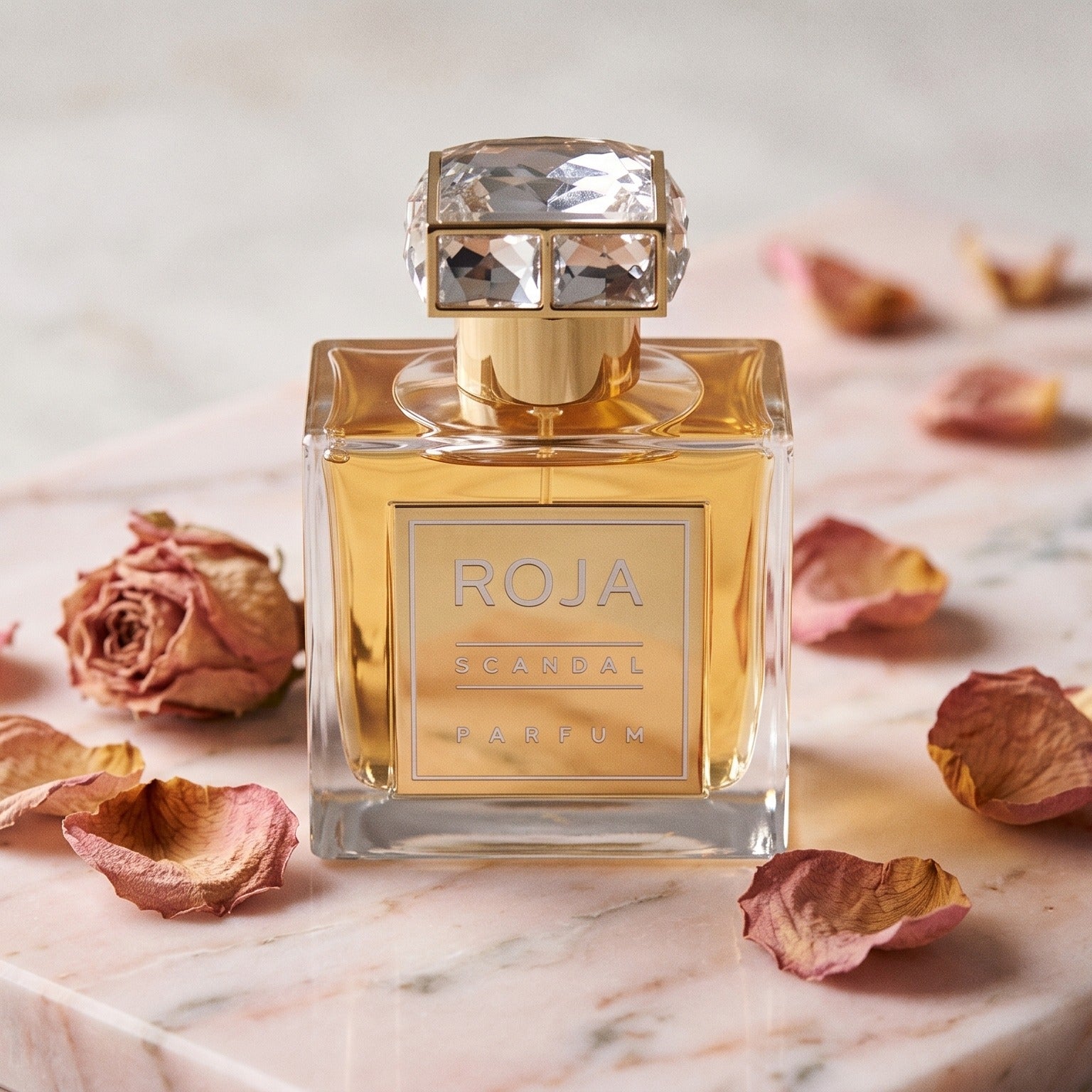 Roja Scandal Pour Femme Parfum on pale pink marble with dried rose petals scattered softly