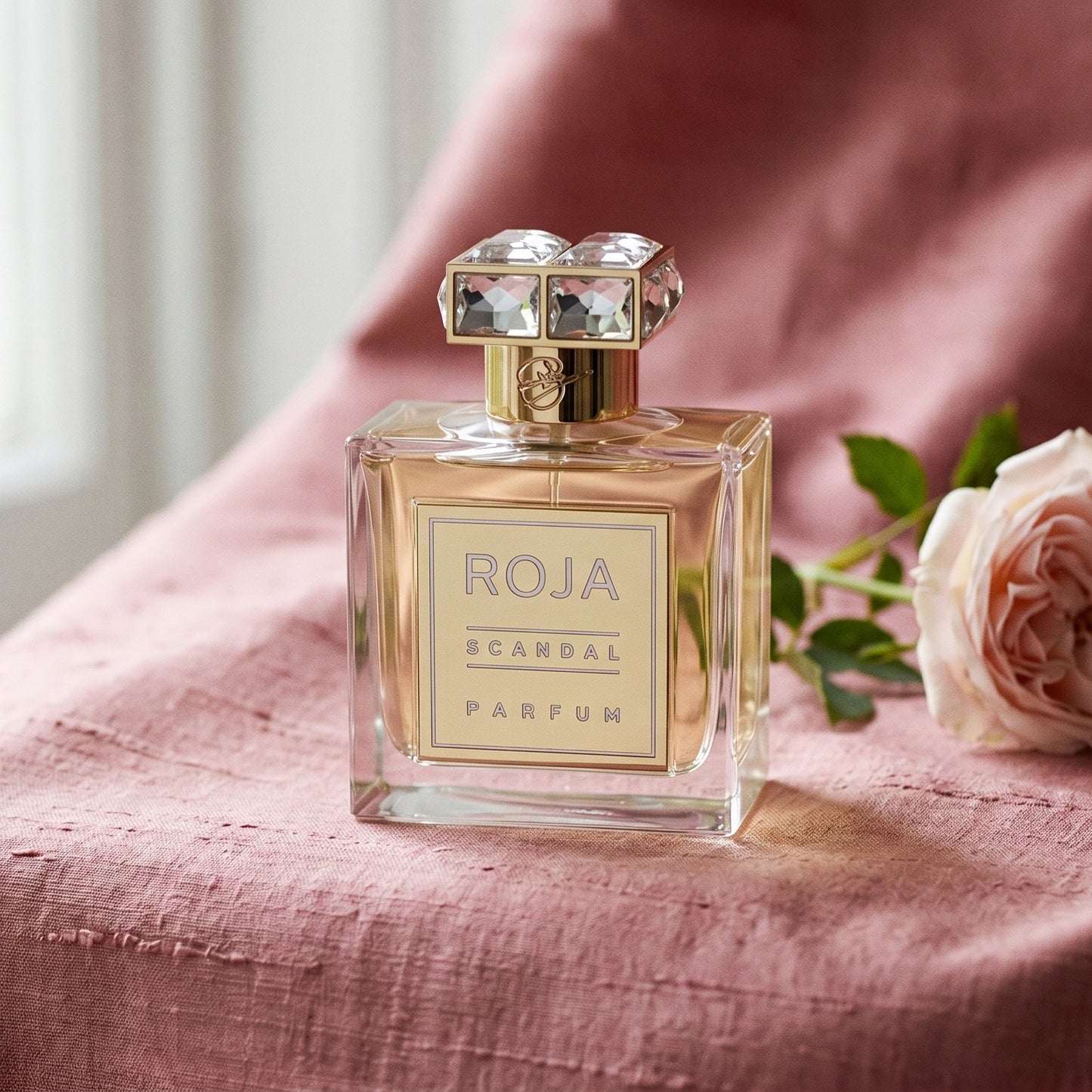 Roja Scandal Pour Femme Parfum on raw silk in dusty pink with a single damask rose stem resting aslant