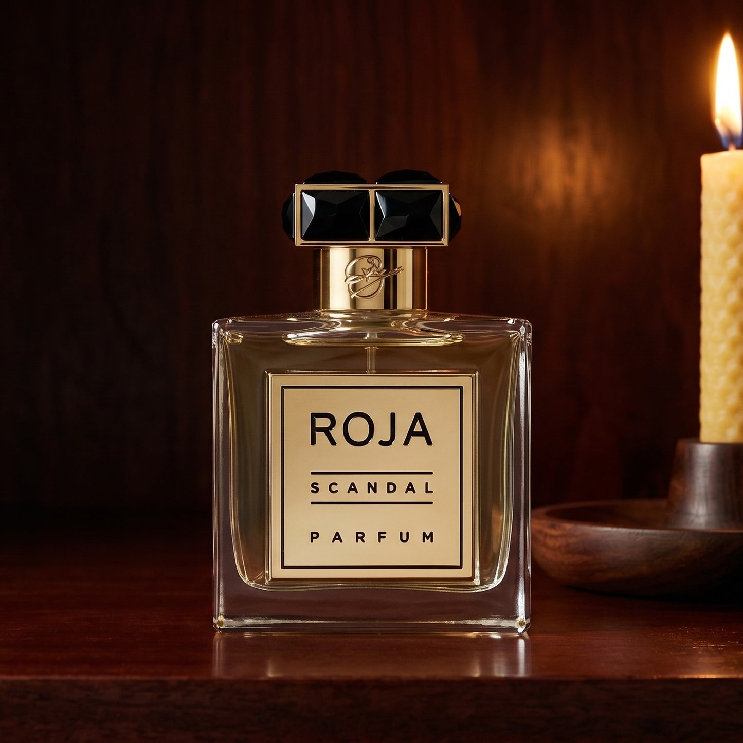 Roja Scandal Pour Homme Parfum on dark cherrywood with a tall beeswax taper casting warm light