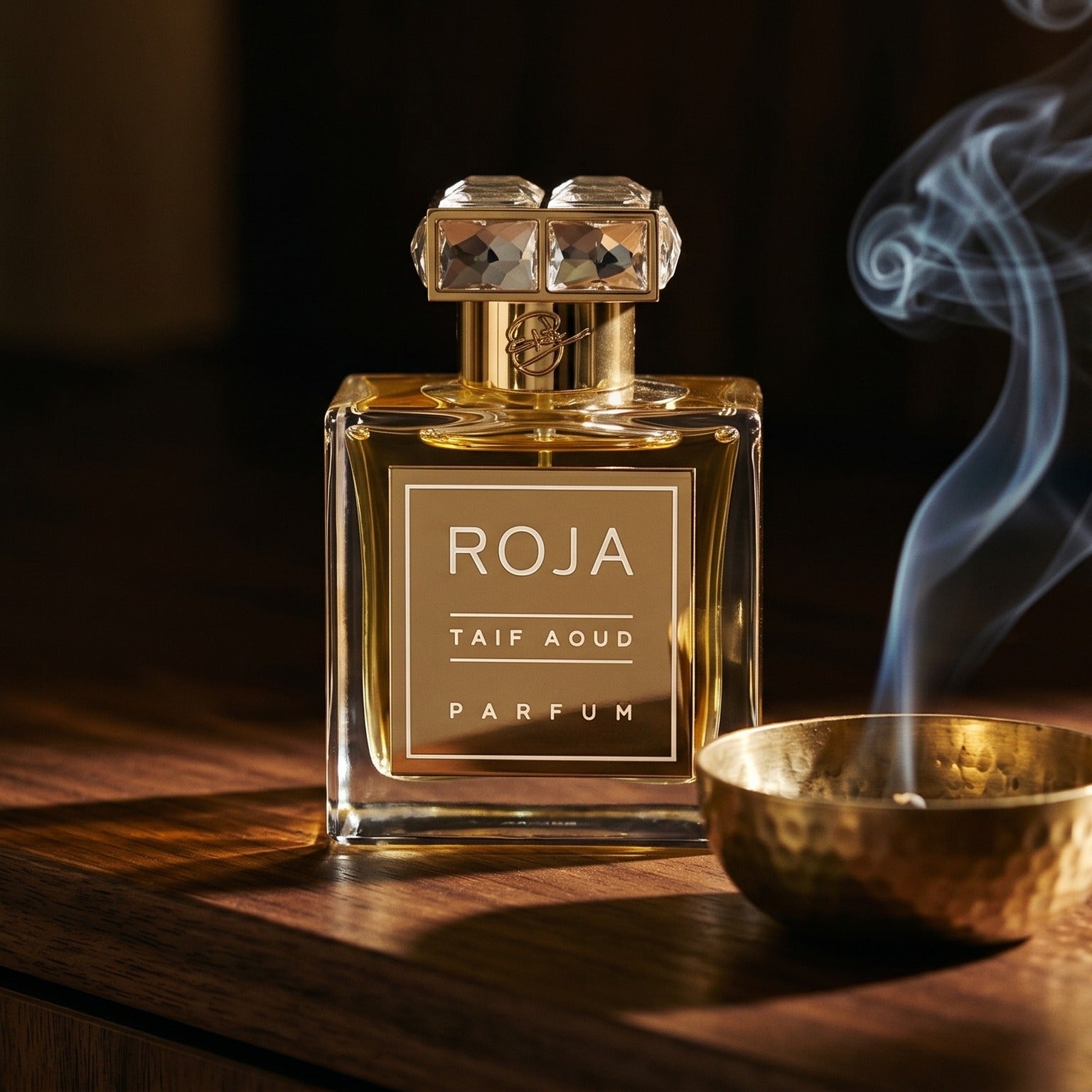 Roja Taif Aoud Parfum on dark walnut console with a small brass incense bowl, smoke curling upward