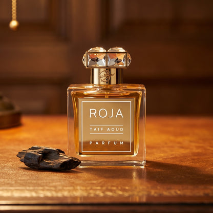 Roja Taif Aoud Parfum on aged leather-topped desk with a single agarwood chip beside the bottle