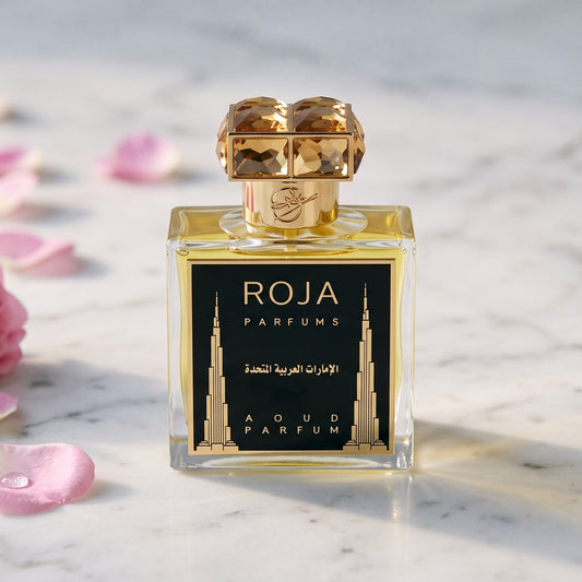 Roja United Arab Emirates Parfum on white marble with fresh Rose de Mai petals scattered to one side
