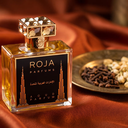 Roja United Arab Emirates Parfum on burnt-orange silk with clove buds and dried jasmine in a small brass saucer