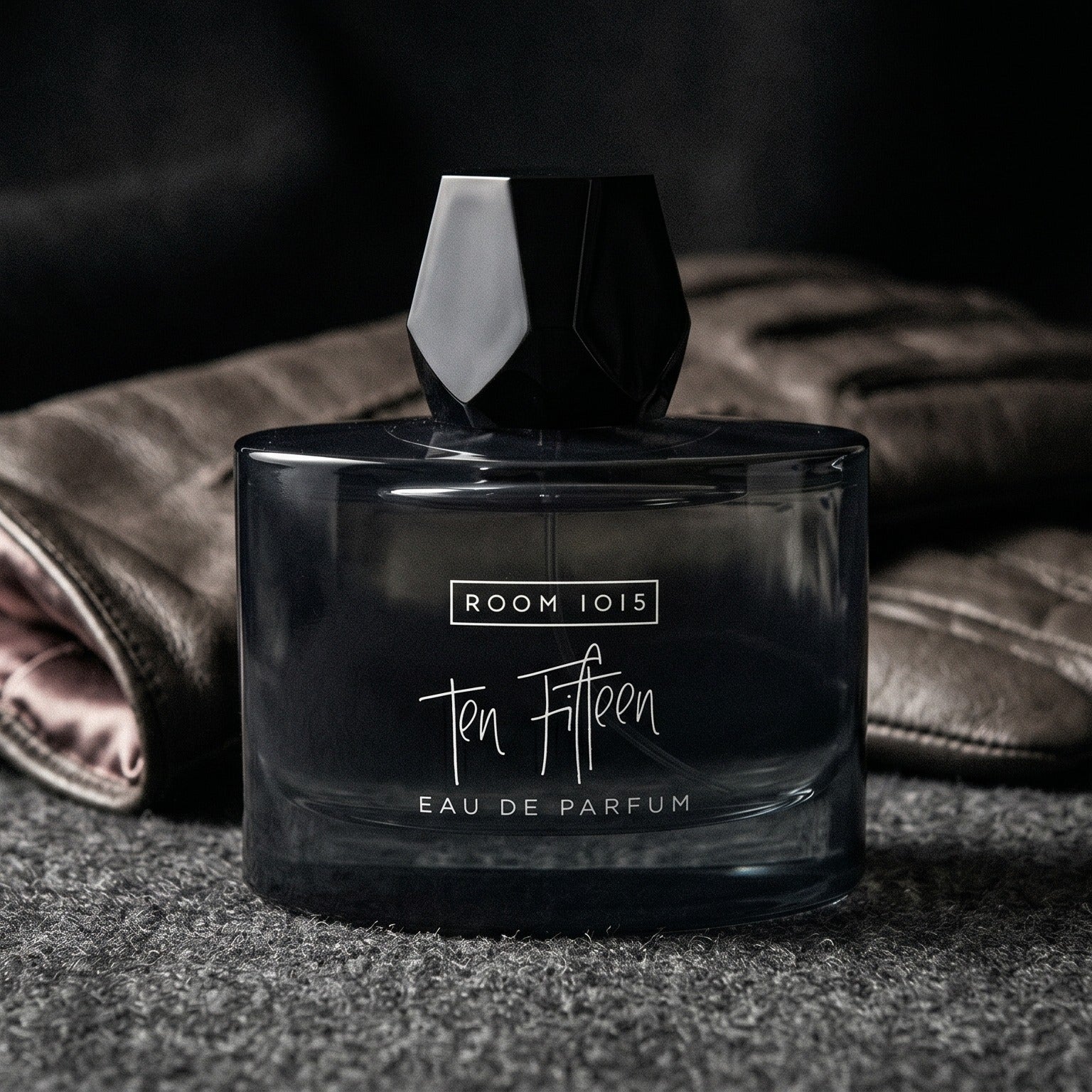 Room 1015 Ten Fifteen EDP on black suede surface with a folded pocket square beside the base
