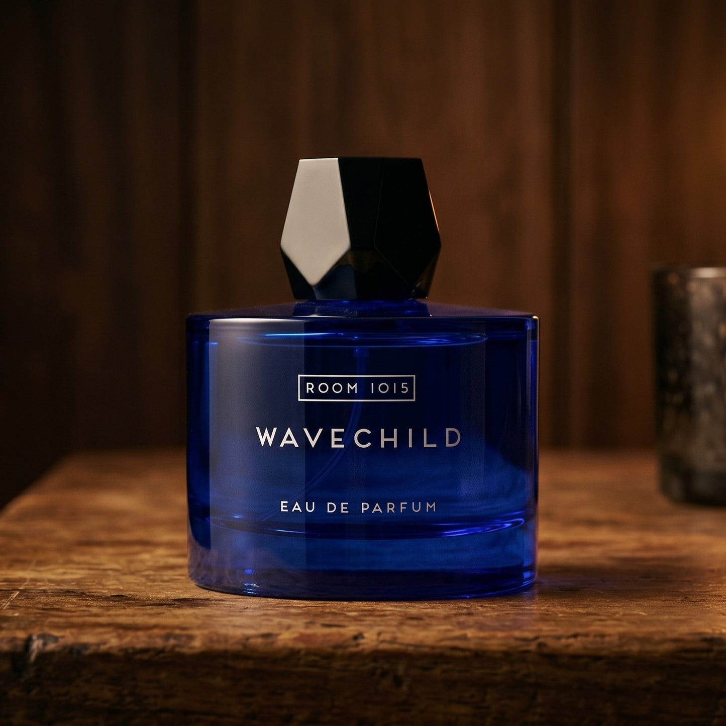 Room 1015 Wavechild EDP on rosewood surface with a squat brass candle flickering nearby