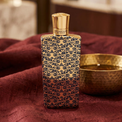 The Merchant of Venice Gold Regatta EDP on deep caramel velvet with a small copper jar of resin balm