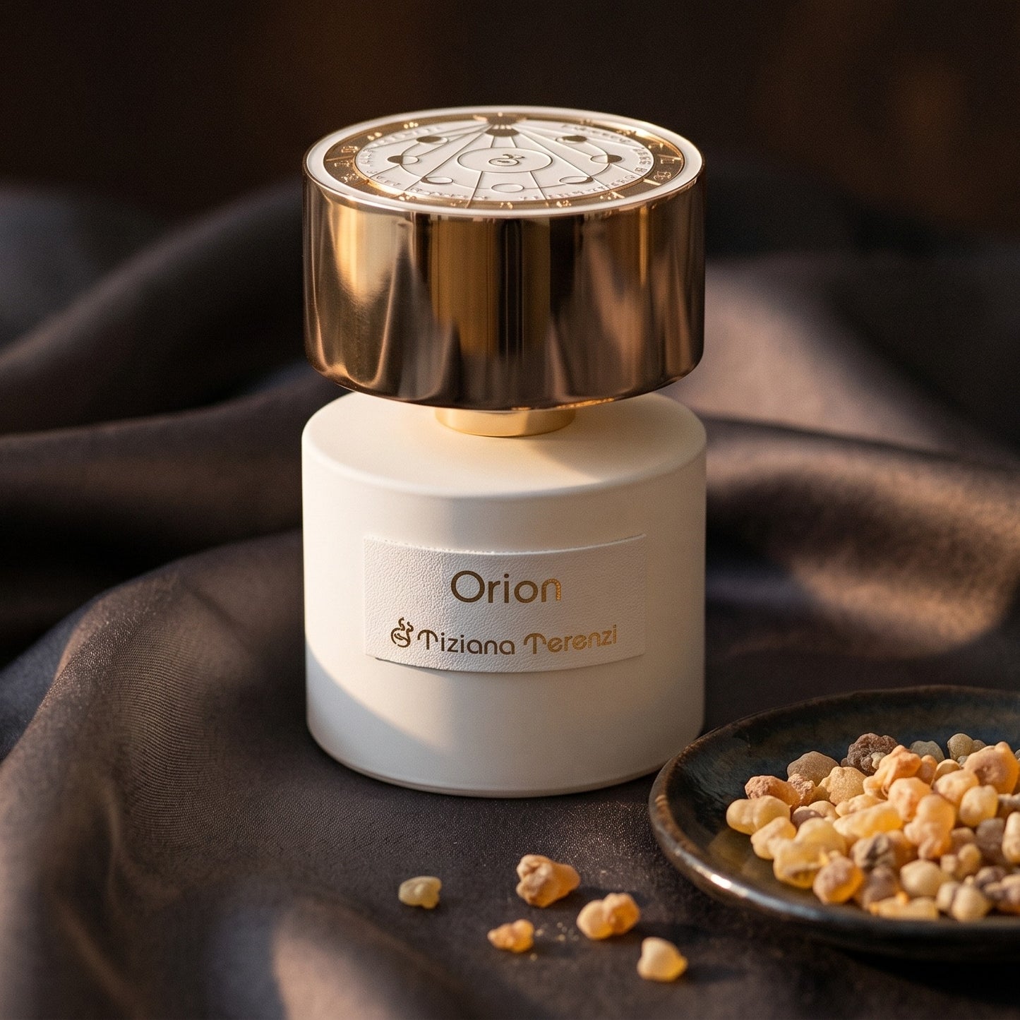 Tiziana Terenzi Orion EDP on burnt-orange silk with smoldering agarwood on a stone dish