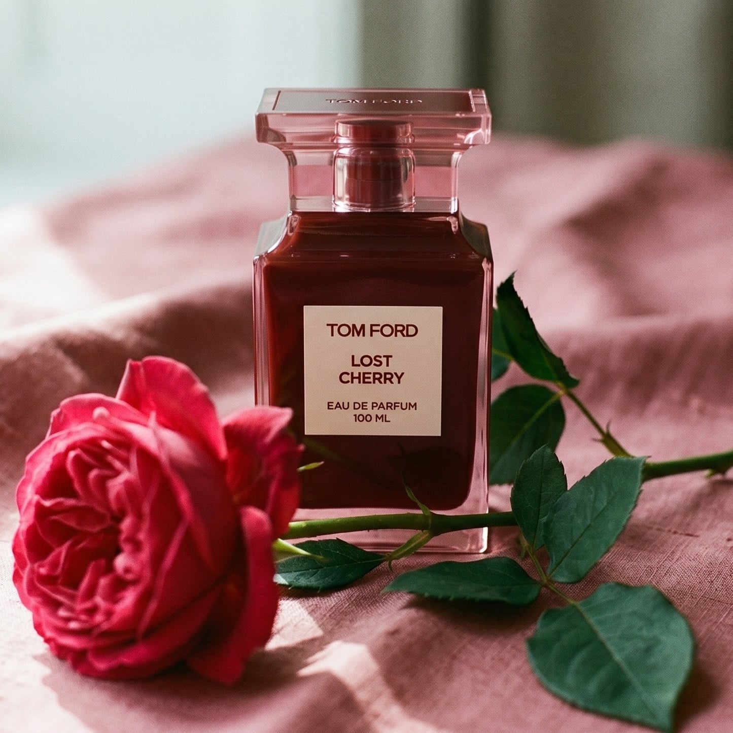 Tom Ford Lost Cherry on mauve linen with a short-stemmed rose placed diagonally