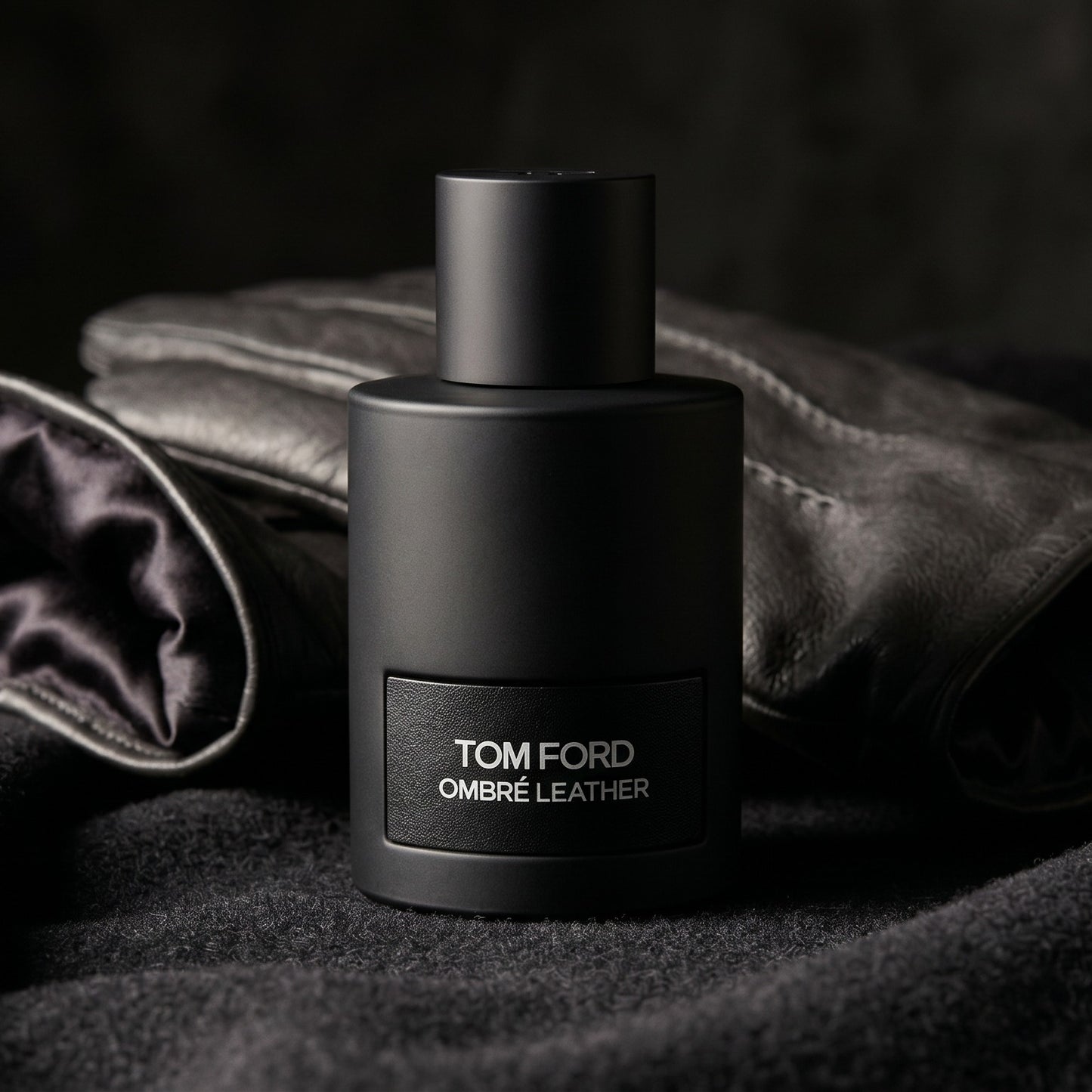 Tom Ford Ombre Leather EDP on black suede surface with a folded pocket square beside the base