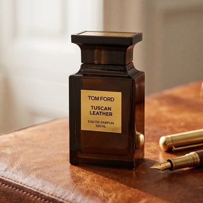 Tom Ford Tuscan Leather on aged cognac-leather surface with a brass fountain pen resting beside the bottle