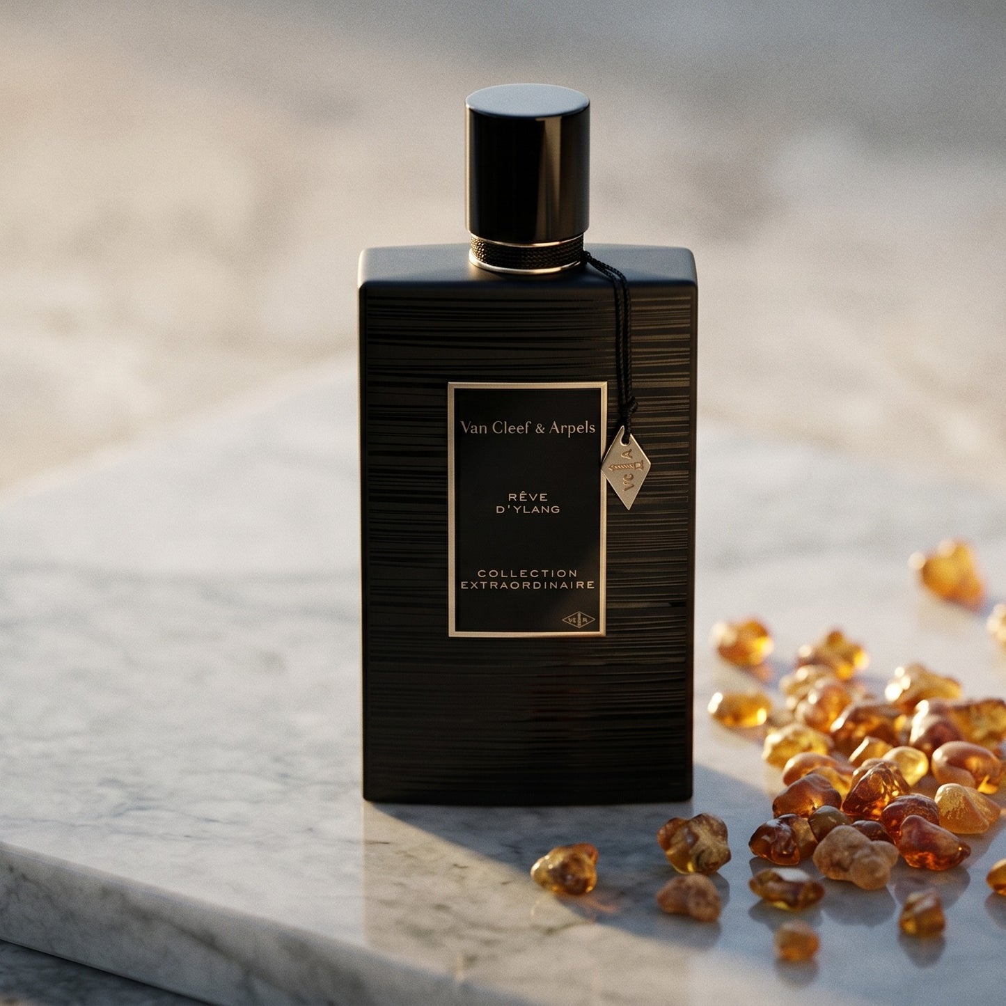 Van Cleef Reve de Ylang on pale grey marble with amber resin beads scattered to one side
