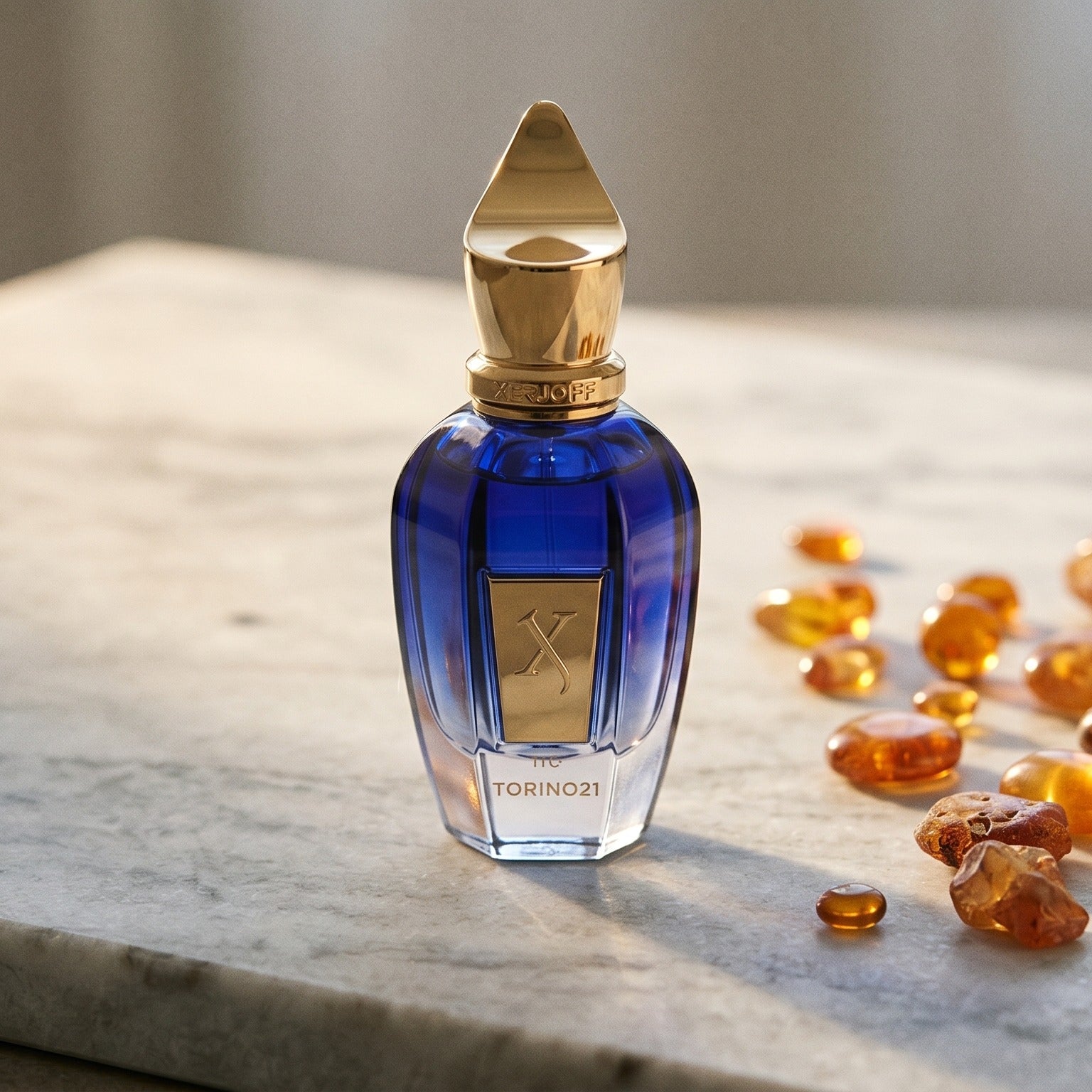 Xerjoff Torino 21 on pale grey marble with amber resin beads scattered to one side