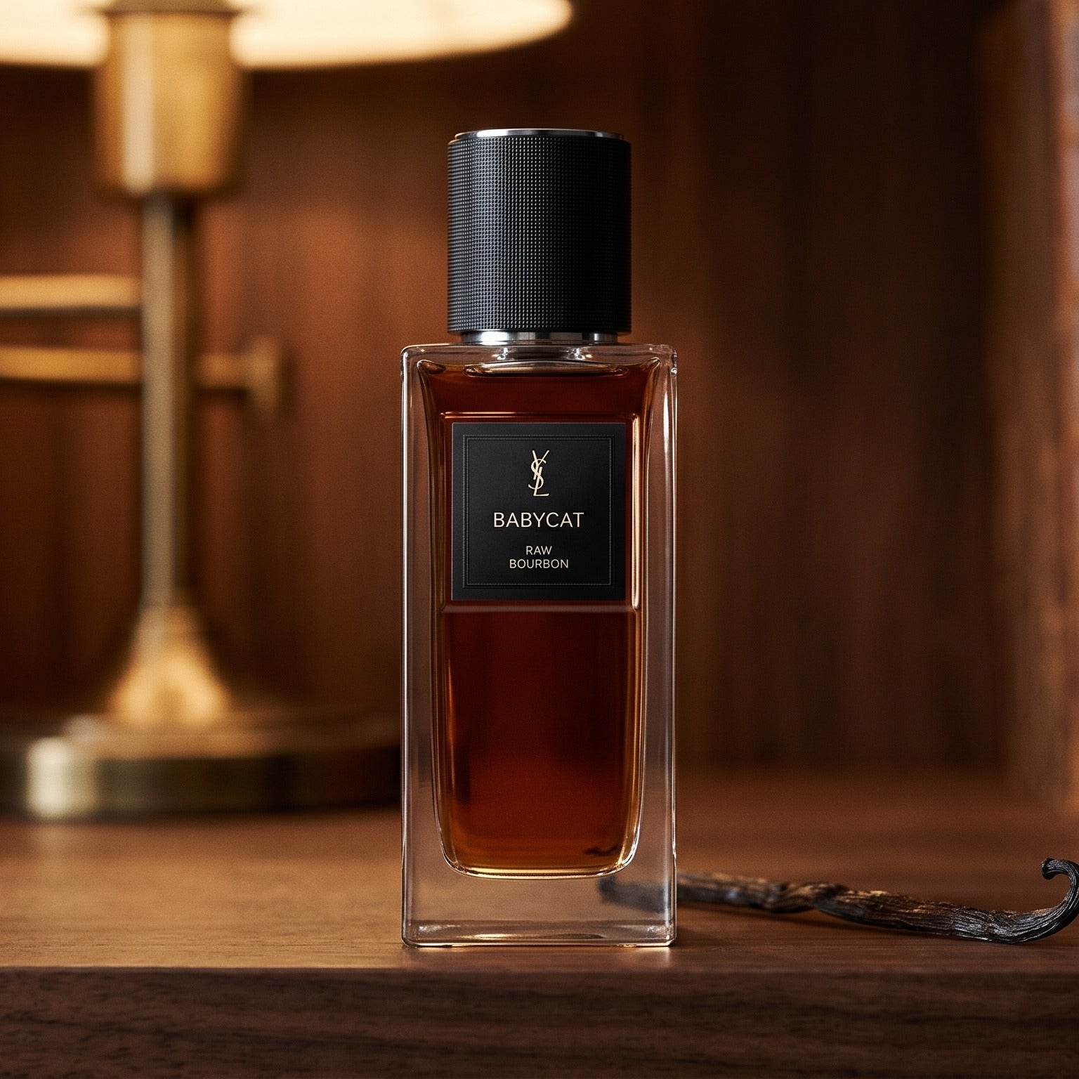 Yves Saint Laurent Babycat Raw Bourbon EDP on dark walnut library shelf with a single vanilla pod resting beside the bottle