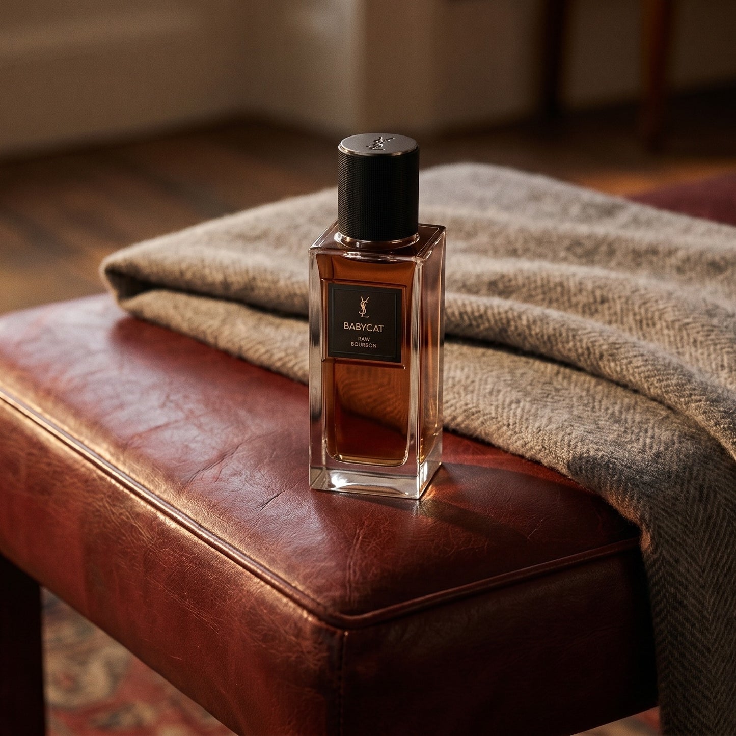 Yves Saint Laurent Babycat Raw Bourbon EDP on oxblood leather footstool with a folded cashmere throw
