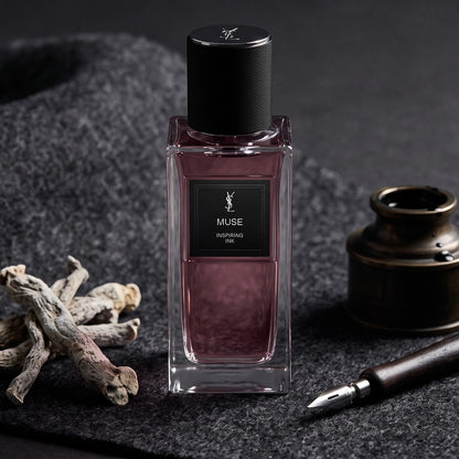 Yves Saint Laurent Muse Inspiring Ink EDP on charcoal felt with an inkwell and a steel nib beside dried iris root